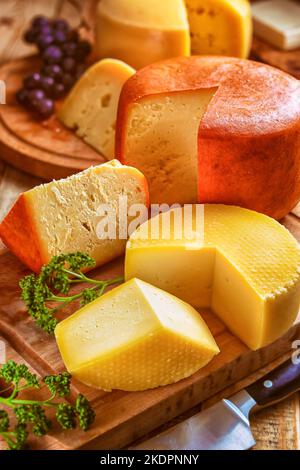 formaggio - vita ferma con vari tipi di formaggio, affettati e serviti pagnotte di formaggi su taglieri a tavola Foto Stock