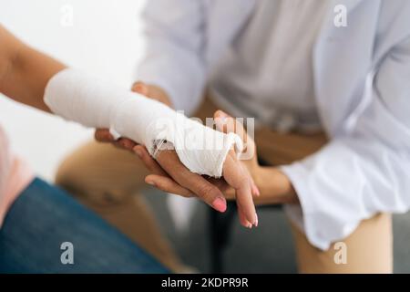 Primo piano ripresa tagliata di irriconoscibile medico ortopedico maschile consulenza paziente femmina ferita con mano rotta avvolto in cerotto al controllo Foto Stock