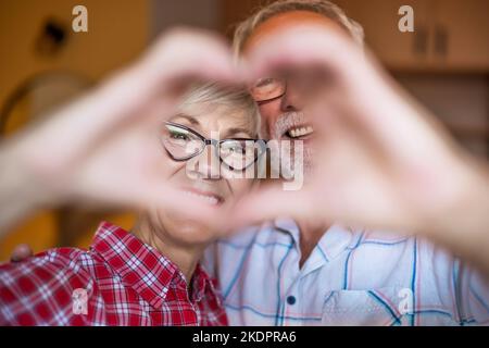 Coppia anziana felice sta abbracciando e facendo la figura del cuore con le loro mani. Foto Stock