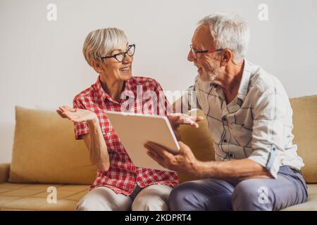 Coppia anziana seduta in salotto e in chat con la famiglia su un tablet digitale. Foto Stock