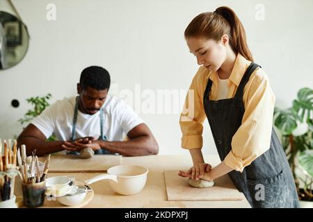 Vista laterale ritratto della giovane donna che forma l'argilla e che dimostra la tecnica alle persone in laboratorio di ceramica studio, copia spazio Foto Stock