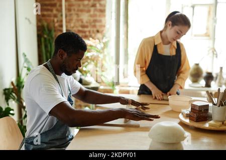 Ritratto con vista laterale di un giovane uomo nero che forma l'argilla mentre si gode una lezione d'arte in studio di ceramica, copia spazio Foto Stock