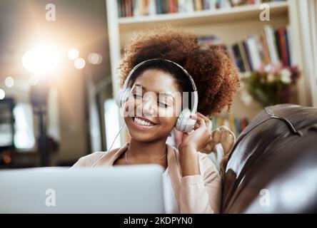 Momenti melodici online. Una giovane donna che si rilassa sul divano e ascolta la musica sul suo laptop. Foto Stock