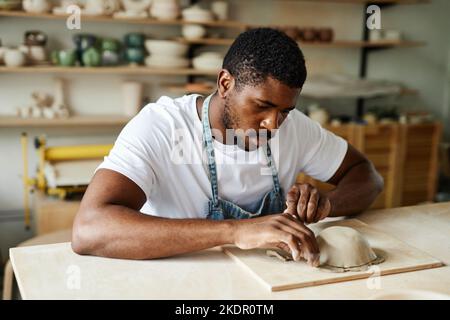 Ritratto dai toni caldi di un creativo uomo nero che forma la ciotola in ceramica in un accogliente studio di ceramica Foto Stock