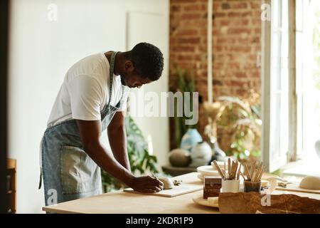 Vista laterale ritratto di giovane afroamericano creazione bella ciotola fatta a mano in accogliente studio di ceramica, spazio copia Foto Stock