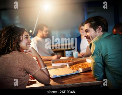 Lavorare tardi ha i suoi vantaggi. Un team di giovani uomini d'affari mangiare la pizza mentre si lavora tardi nel. Foto Stock