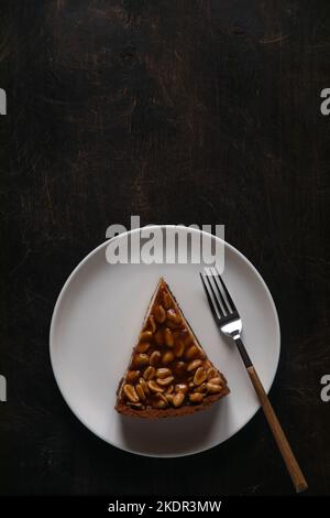 Cheesecake fatta in casa con caramello e arachidi su sfondo scuro. Deliziosa torta da forno al mattino. Foto Stock