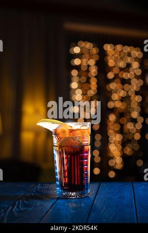 Bicchiere di cocktail al bar su sfondo luminoso e sfocato. Cocktail alcolico con Coca-Cola, limone decorato. Foto Stock