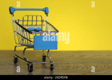 Mini carrello su sfondo giallo con spazio per le copie. Concetto di shopping e di consumo. Foto Stock