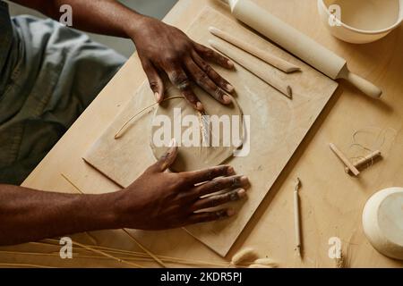 Vista dall'alto primo piano di ceramiche artigianali maschili che decorano a mano con impronta vegetale utilizzando grano, spazio copia Foto Stock