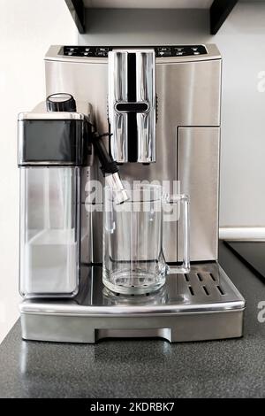 Macchina da caffè color acciaio per preparare diversi tipi di caffè con tazza in vetro sul supporto. Preparazione per la preparazione del caffè Foto Stock