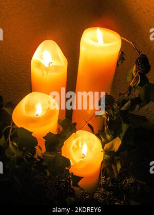 Candele dell'Avvento, accese di notte, circondate da foglie e semi secchi. Foto Stock