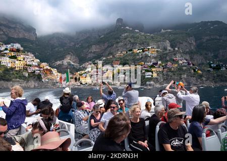 La città di Amalfi, sulla costiera amalfitana, che mostra un cielo azzurro e un sole limpidi. Preso da una barca che lascia la città con i viaggiatori presenti. Foto Stock