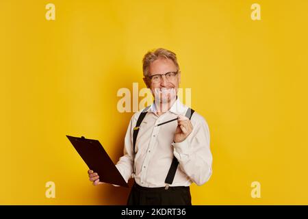 Ritratto dell'uomo maturo in abiti classici di stile in posa isolata su sfondo giallo studio. Professore Foto Stock