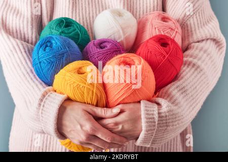 Donna che detiene filati di lana colorati o multicolore su sfondo blu. Molte sfere multicolore di fili primo piano. Concetto di lavorazione a maglia o a cucito. Foto Stock