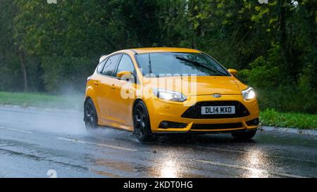 Ford Focus 2014 gialla guida sotto la pioggia su strade bagnate Foto Stock