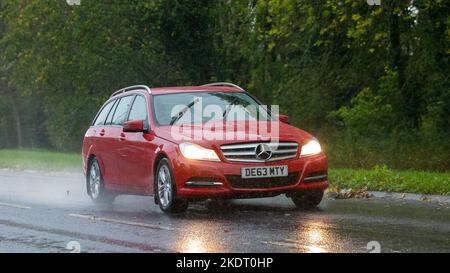Mercedes Benz 2013 rossa modello C guida sotto la pioggia su una strada bagnata Foto Stock