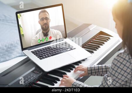 Musicista giovane e grazioso che suona il pianoforte digitale classico a casa durante la lezione online a casa, distanza sociale durante la quarantena, autoisolamento, online Foto Stock