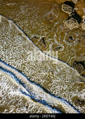 Vista dall'alto verso il basso delle onde che si infrangono su una spiaggia di sabbia con grandi massi (Southerndown, Galles) Foto Stock