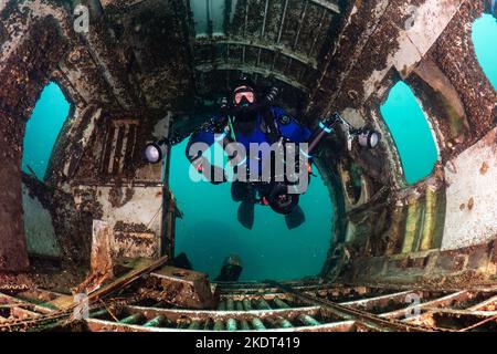 Scuba diver su un circuito chiuso rebreather e fotocamera subacquea nuotare attraverso un vecchio relitto aereo sott'acqua Foto Stock