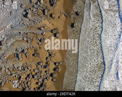 Vista dall'alto verso il basso delle onde che si infrangono su una spiaggia di sabbia con grandi massi (Southerndown, Galles) Foto Stock