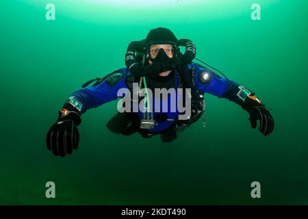 SCUBA subacqueo in un drysuit e respira sott'acqua in una cava fredda, scura e torbida Foto Stock