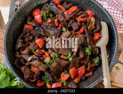 Soffriggere il manzo con le verdure in una padella su sfondo rustico Foto Stock