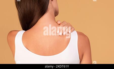 Giovane donna caucasica che soffre di dolore acuto alla spalla, toccando la zona dolorosa e massaggiandola, panorama Foto Stock