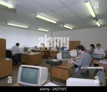 1980s, storico, vista attraverso un ufficio aperto dell'epoca, dipendenti di sesso maschile e femminile che lavorano alle scrivanie, utilizzando piccoli terminali computer da tavolo, probabilmente realizzati da IBM, Inghilterra, Regno Unito. Essendo monitor CRT, visualizzavano il testo in verde, come si vede nell'immagine, diventando così noti come terminali con schermo verde. Foto Stock