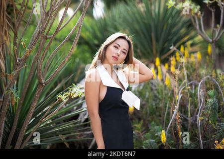 Bella giovane donna che indossa un abito corto bianco e nero in piedi in un giardino di Cactus | scena nel deserto Foto Stock