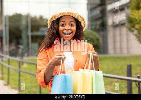 Allegro scioccato emotivo bella donna nera millenaria in cappello apre un sacco di pacchetti con gli acquisti, gode acquistare Foto Stock