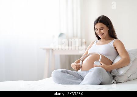 Donna incinta positiva che tiene le cuffie sulla pancia grande, panorama Foto Stock