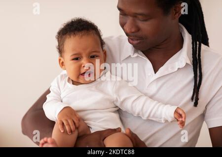 Concetto di paternità. Padre premuroso che tiene il bambino nero piangendo piccolo sulle mani Foto Stock