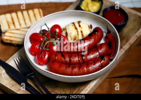 Salsicce bavaresi alla griglia con mozzarella e pomodori ciliegini in un piatto con salse. Foto Stock