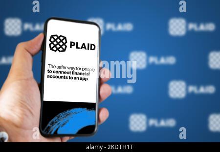 San Francisco, USA, giugno 2022: Tenere in mano un telefono con la home page di Plaid sullo schermo. Logo a plaid ripetuto sfocato su sfondo blu. Plaid è un financ Foto Stock