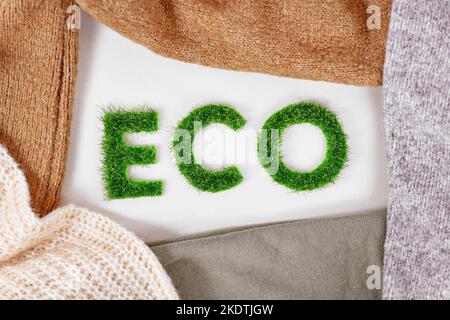 Concetto di abbigliamento prodotto rispettoso dell'ambiente con testo 'ECO' fatto di erba circondata da tessuti Foto Stock