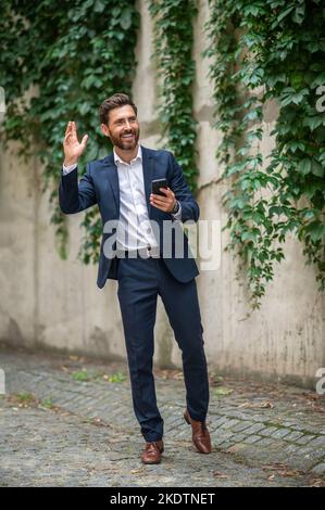 Elegante giovane uomo che saluta qualcuno e agitando la mano Foto Stock