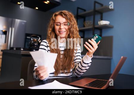 Donna felice che utilizza l'app di online banking per pagare le fatture, tenere assegni. Reddito di contabilità femminile, debiti, prestiti, riceventi per pagare le tasse con fintech Foto Stock