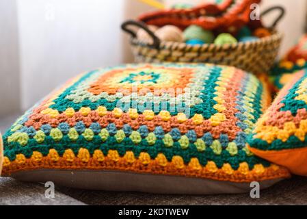 Uncinetto quadrato Granny. Creazioni fatte in casa. Filati di lana colorati in un cesto di paglia su un divano. Lavorazione a maglia fatta a mano, cuscini in maglia e un'atmosfera carina. Foto Stock