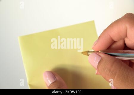 Mano della donna con le unghie verniciate che tengono la carta bianca della lettera su fondo bianco puro. Foto Stock