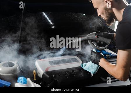 Processo di pulizia a vapore del motore dell'auto da polvere e sporcizia. Lavaggio a vapore del motore di auto nei dettagli del servizio auto Foto Stock