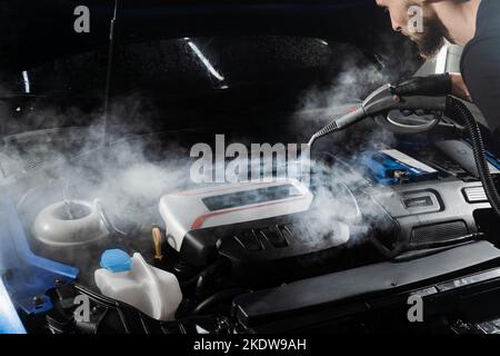 Processo di pulizia a vapore del motore dell'auto da polvere e sporcizia. Lavaggio a vapore del motore di auto nei dettagli del servizio auto Foto Stock