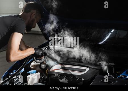 Lavaggio a vapore del motore di auto nei dettagli del servizio auto. Processo di pulizia a vapore del motore dell'auto da polvere e sporcizia Foto Stock