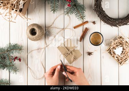 Donna tagliata mani corda da taglio per cartone confezionato in decorazione natale di cannella, regali e abete ramo e corona. Avvolgimento naturale e. Foto Stock