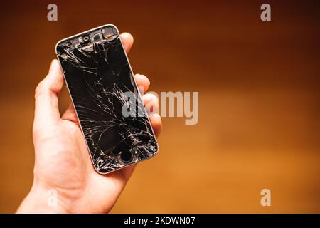 Persona che tiene in mano smartphone rotto con schermo incrinato Foto Stock
