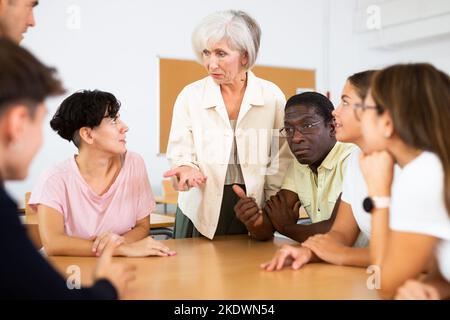 Donna anziana che partecipa a un club di lingua inglese con un gruppo multirazziale di persone Foto Stock