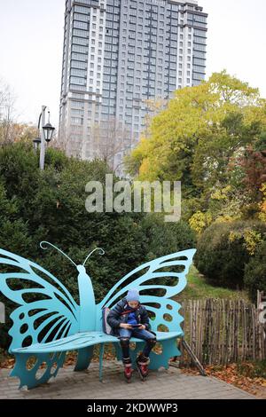 Un ragazzo è visto seduto su una panca a forma di farfalla sullo sfondo di un alto edificio nel Giardino Botanico sul Boulevard Francese. Giardino Botanico dell'Università Nazionale di Odessa, che prende il nome da Ilya Mechnikov. Sul territorio del giardino si presentano più di 3.000 tipologie di spazi verdi con una superficie di circa 16 ettari. Il giardino è una suddivisione educativa della Facoltà di Biologia dell'Università, sulla base dei diplomi e delle relazioni terminologiche vengono svolti annualmente, il personale scientifico del giardino partecipa al processo educativo. Nel 1963, l'Orto Botanico fu dato t Foto Stock