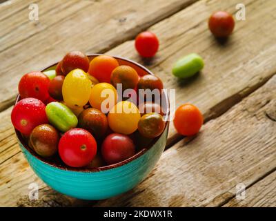 Pomodori freschi e colorati in una ciotola blu su un tavolo da cucina in legno. Composizione culinaria colorata. Stile country. Non ci sono persone nella foto. Cuoco Foto Stock