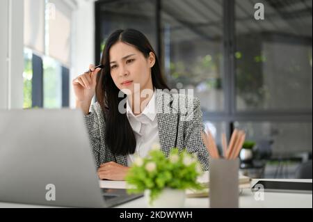 Affascinante e premuroso giovane donna d'affari asiatica o manager femminile pensare e pianificare nuove idee per la sua attività. Foto Stock