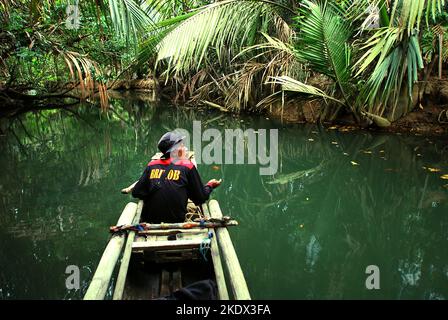 Un ranger del parco nazionale che indossa una giacca Brimob (Indonesian Mobile Brigade Corps) sta pescando dalla barca sul fiume Cigenter, mentre sta facendo una pausa dal viaggiare attraverso la foresta costiera dell'Isola di Handeuleum nel Parco Nazionale di Ujung Kulon, Pandeglang, Banten, Indonesia. Foto Stock